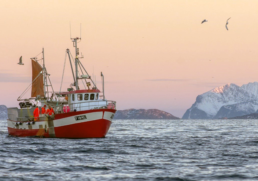 Fiskebåt på havet med fjell i bakgrunnen.