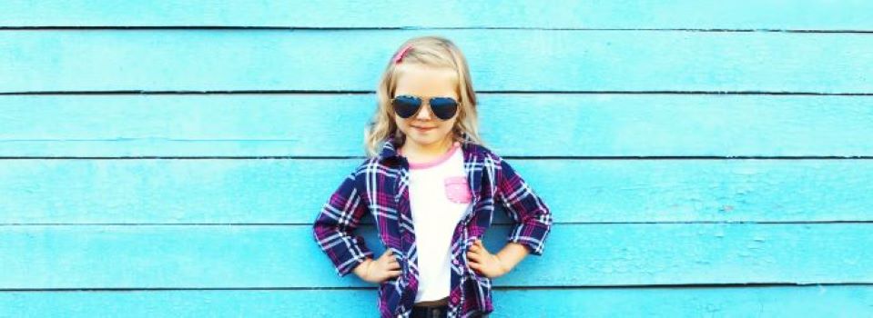 Bilde av en jente som har stilt seg opp foran en blå vegg med solbriller